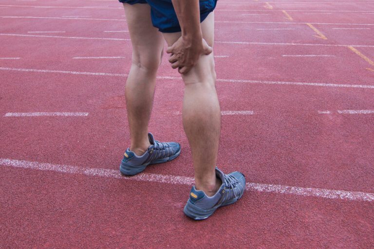 Pernas masculina com a mão no ligamento cruzado posterior indicando dor.
