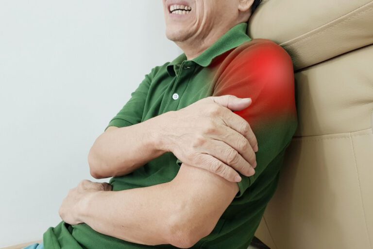 Homem segurando um dos braços e há uma ilustração avermelhada no local do ombro, sinalizando dor.
