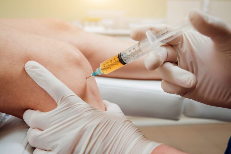 Médico aplicando injeção em joelho de paciente.